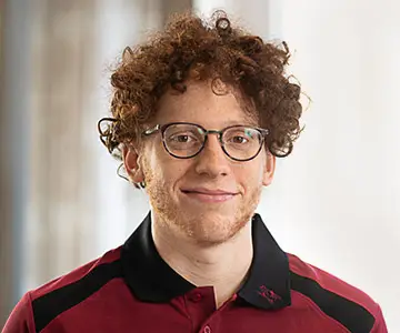 Ein junger Mann etwa Ende zwanzig, mit Brille, roten krausen Haaren und einem roten kurzen Bart.