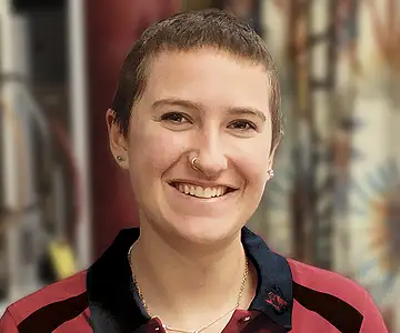 Eine junge Frau etwa Mitte zwanzig mit sehr kurzen braunen Haaren und einem kleinen goldenen Ring in der Nase.