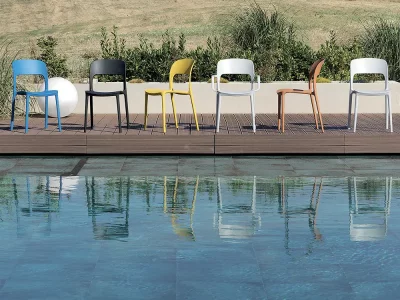 Stühle in verschiedenen Farben stehen auf einer Holzterrasse vor einem Wasserteich. Die Stühle sind von verschiedenen Seiten zu sehen.