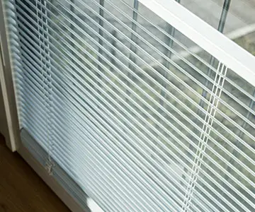 Nahaufnahme eines innenliegenden, weißen Lamellen-Rollos an einem Fenster.